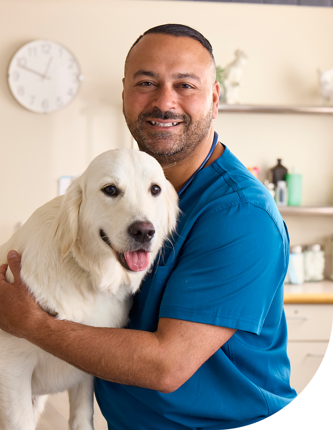 Dr. James Bascharon in blue scrubs hugging a white dog in a vet office